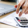Reducão de custos em ti sendo ilustrada com uma imagem de uma pessoa fazendo cálculos com uma calculadora na frente de um notebook.