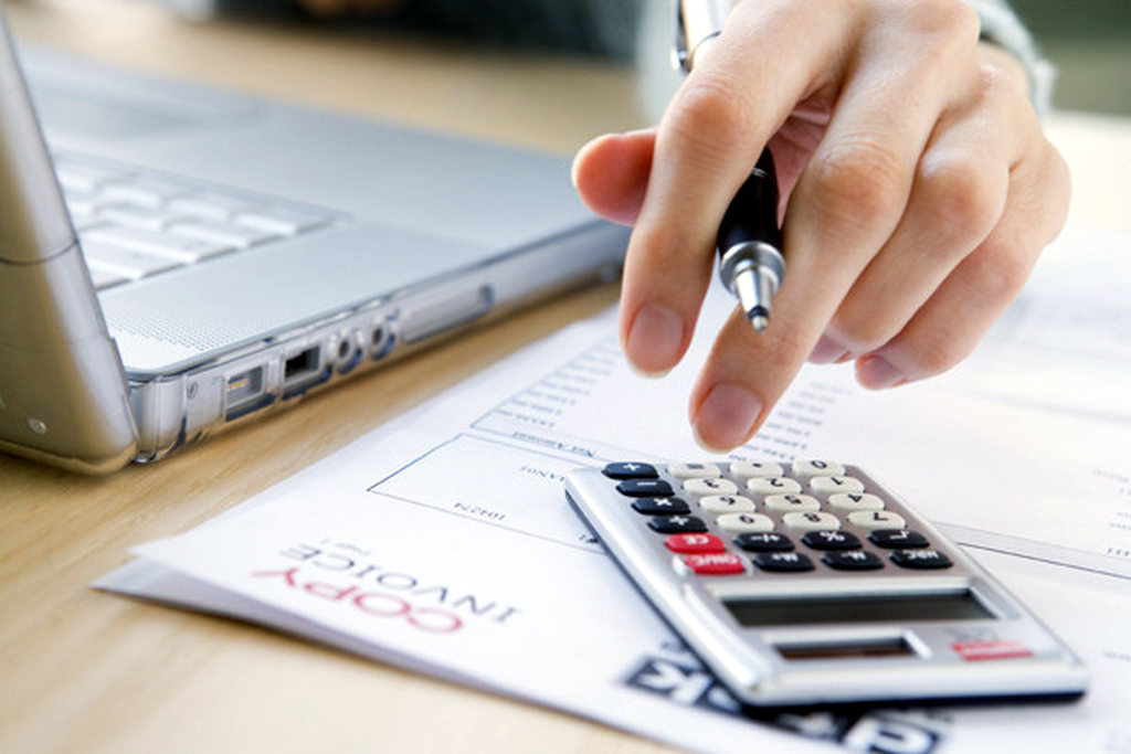 Reducão de custos em ti sendo ilustrada com uma imagem de uma pessoa fazendo cálculos com uma calculadora na frente de um notebook.